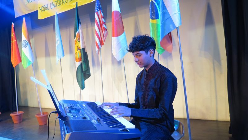 A student plays keyboard at the opening ceremony beneath a row of national flags.