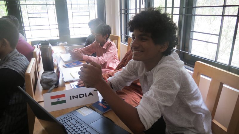A delegate representing India looks up from a laptop across the committee table.