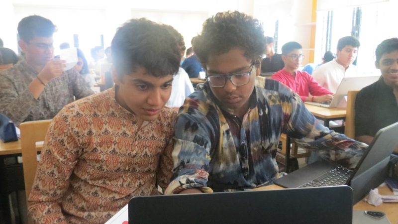 Two delegates draft a clause together on a laptop.